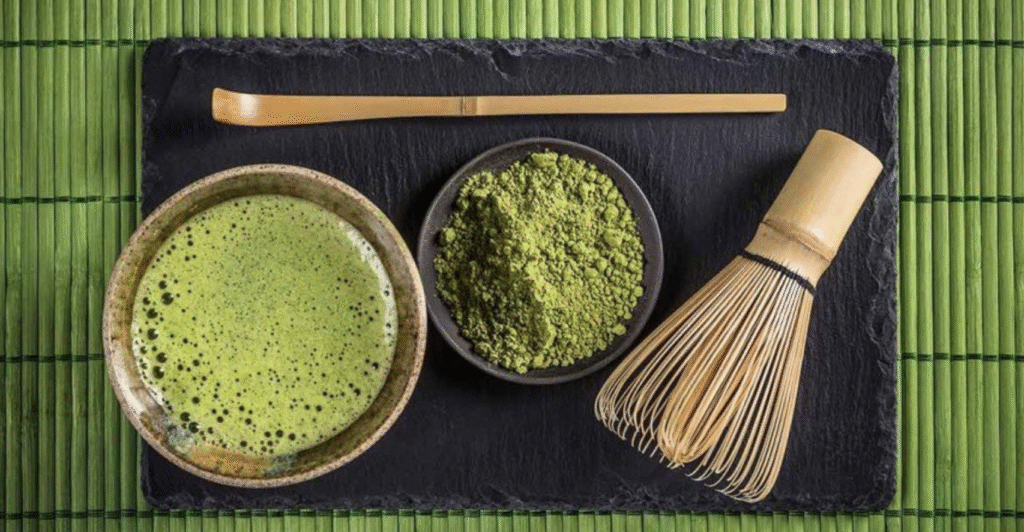 Taza de matcha verde espumoso con polvo de té japonés y utensilios tradicionales de bambú